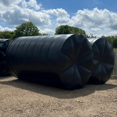 Three 25000 litre black MDPE tanks lying on their side on gravel, with base visible.