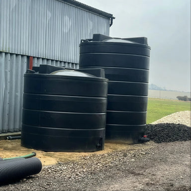 Side view of large, black MDPE split rainwater harvesting tanks on a farm: 13,000 litre tank in front of a 20,000 litre tank, forming a total of 33,000 litres of water storage, fed by rooftop catchment from Ecosure.

